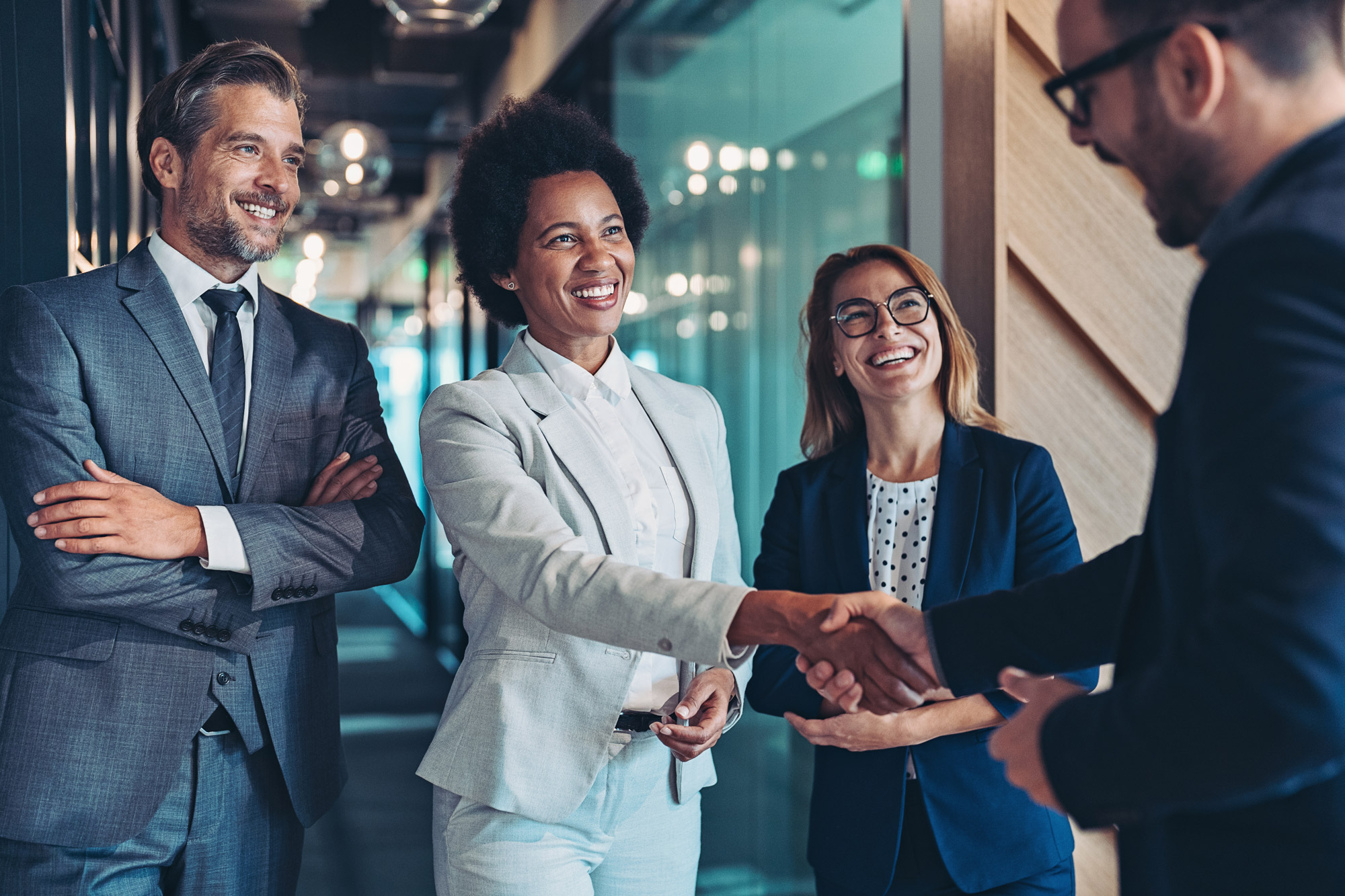 A man shaking hands with one of a group of smiling coworkers.